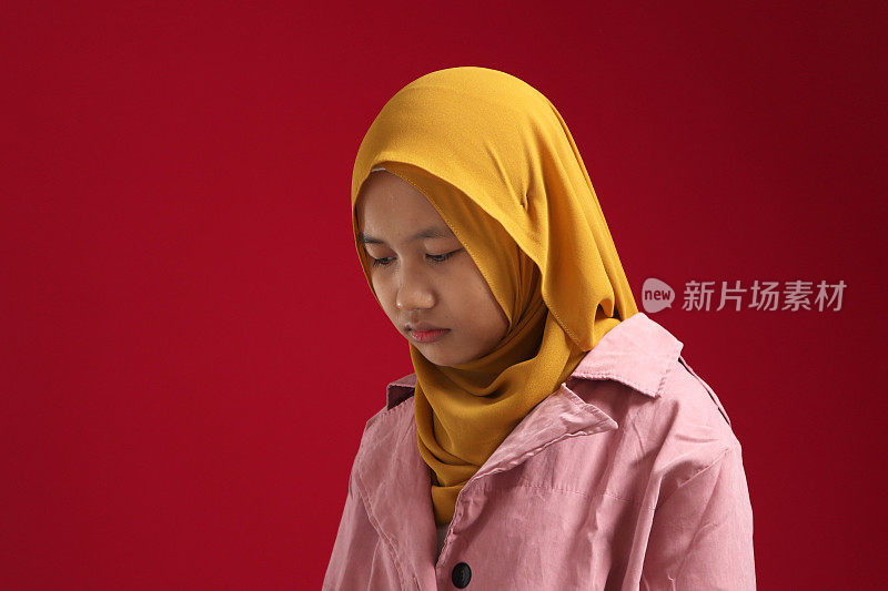 Portrait of sad young Asian teenage muslim girl wearing hijab looking down and depressed